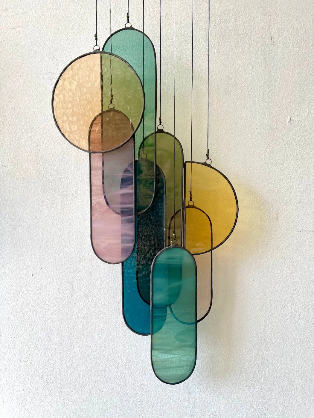 Barra stained glass art with overlapping oval and circular panels in soft teal amber rose and yellow hues with textured patterns
