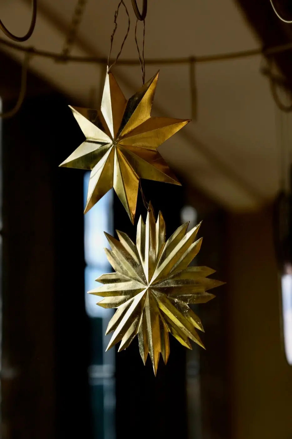 Golden star-shaped paper ornaments hanging from a string set of 2 bras star decorations for festive use