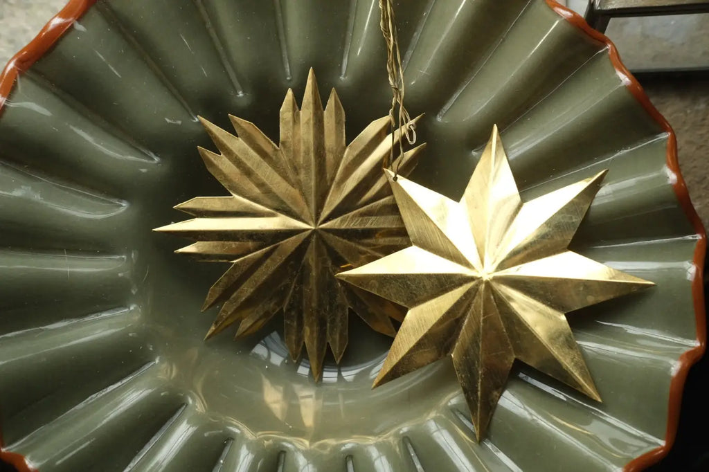 Two golden star-shaped metal bras star decorations resting inside a green ceramic bowl set of 2
