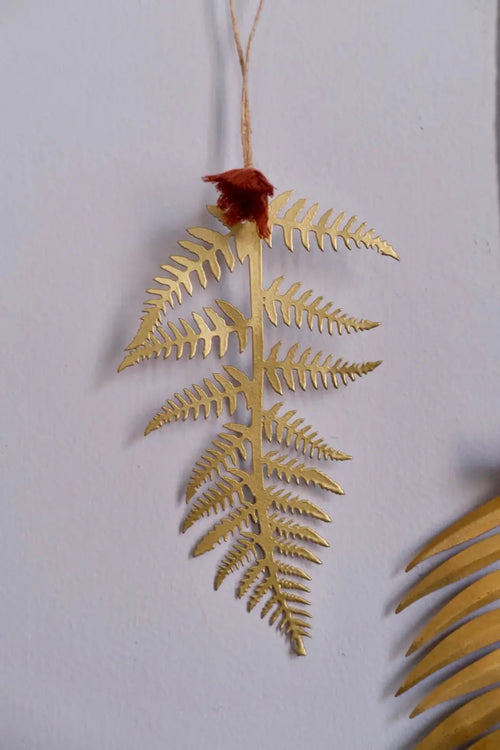 Brass fern leaf decoration in gold metal with rustic twine hanger and red fabric accent at the stem
