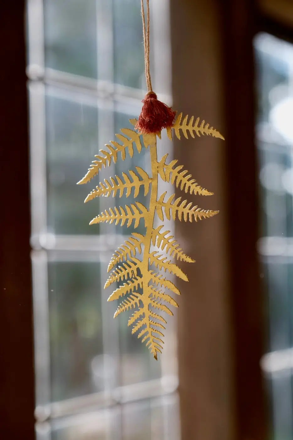 Brass fern leaf decoration featuring a golden fern-shaped ornament with a red tassel at the top