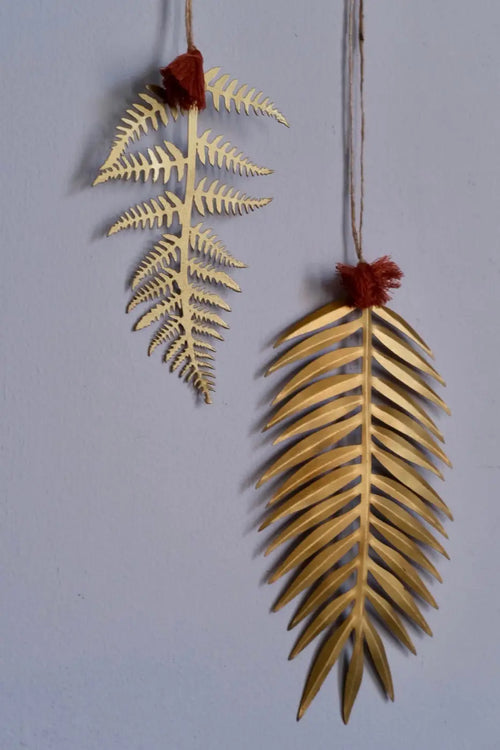 Two golden brass fern leaf decorations with red tassels hanging as elegant holiday ornaments