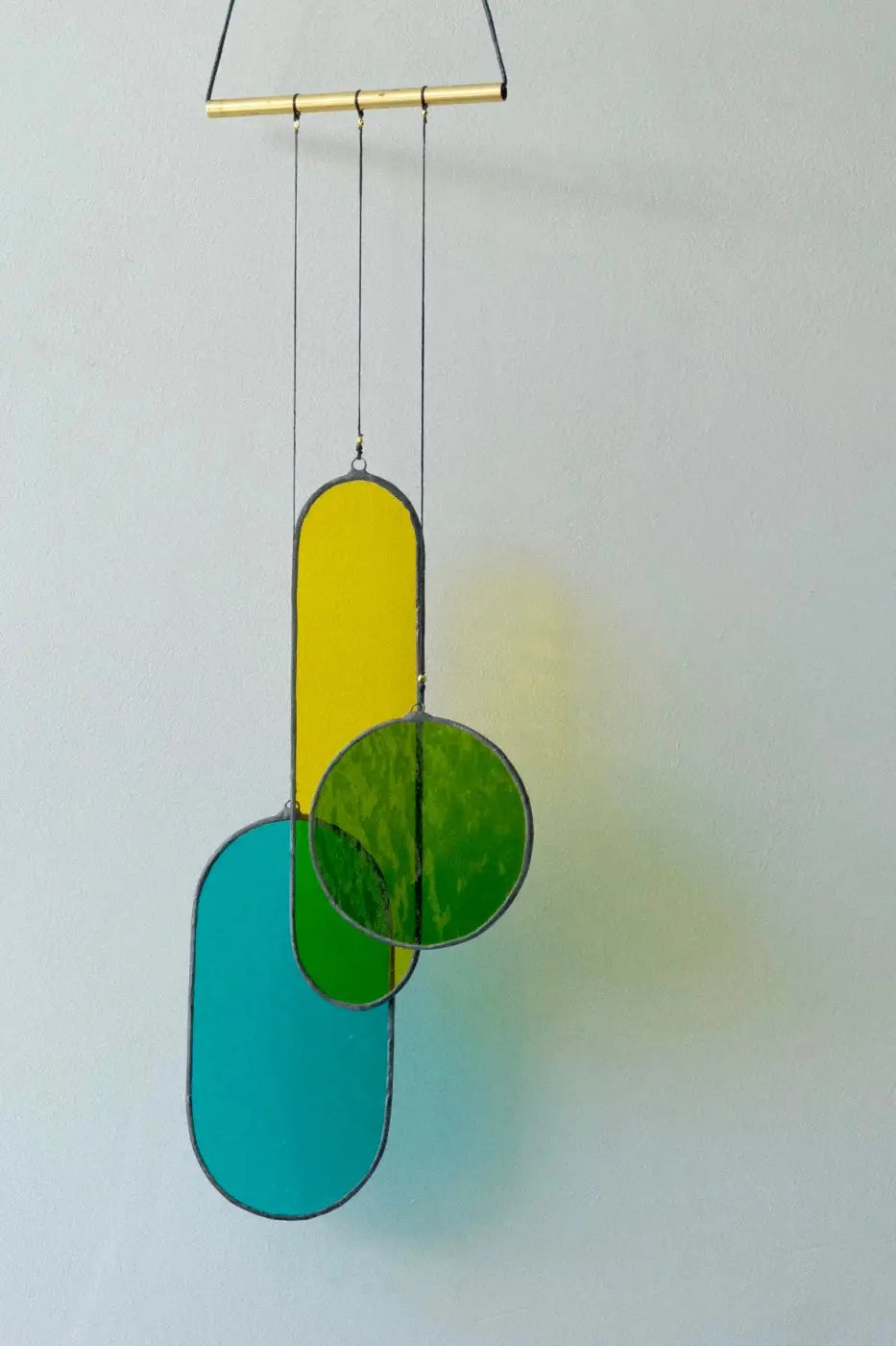 A modern stained glass hanging mobile with vibrant yellow green and teal geometric design and black leaded edges