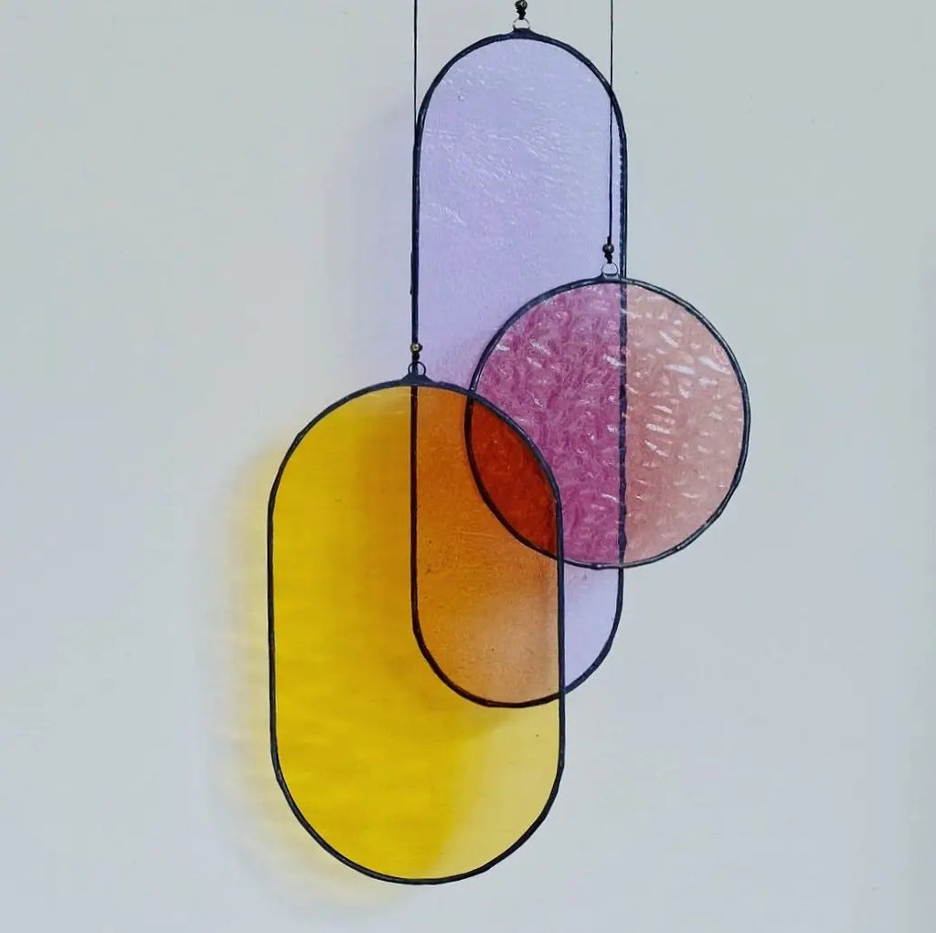 A circa stained glass art piece with overlapping oval and circular panels in yellow lavender pink and orange hues