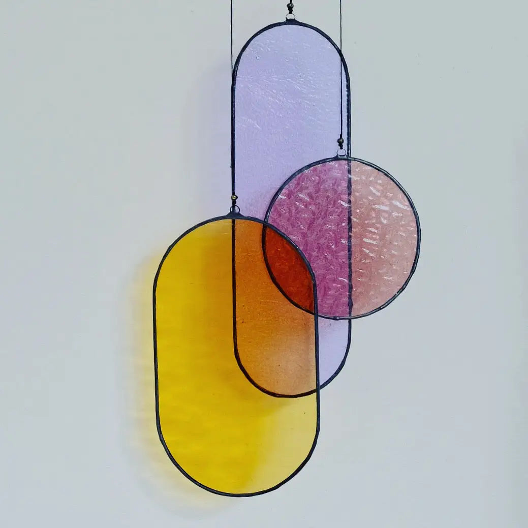 Three hand cut, copper foiled stained glass shapes with a black patina finish, hung with hemp cord from a brass hoop.