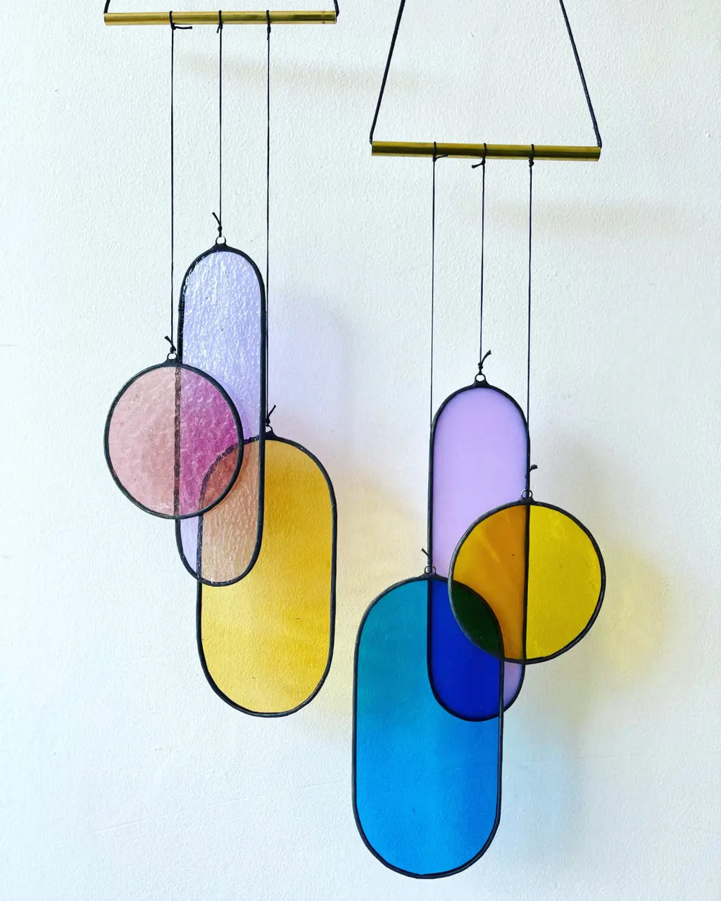 Vibrant geometric stained glass mobiles with pastel and bold panels suspended from brass rods by Circa Stained Glass Art