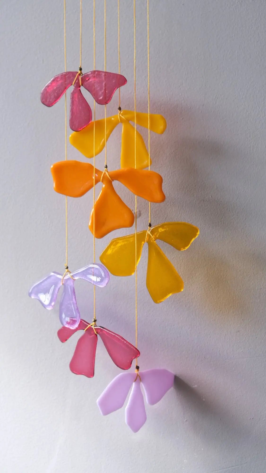 A colorful glass flower mobile with translucent petals in shades of pink, yellow, orange, and purple hanging from thin strings.