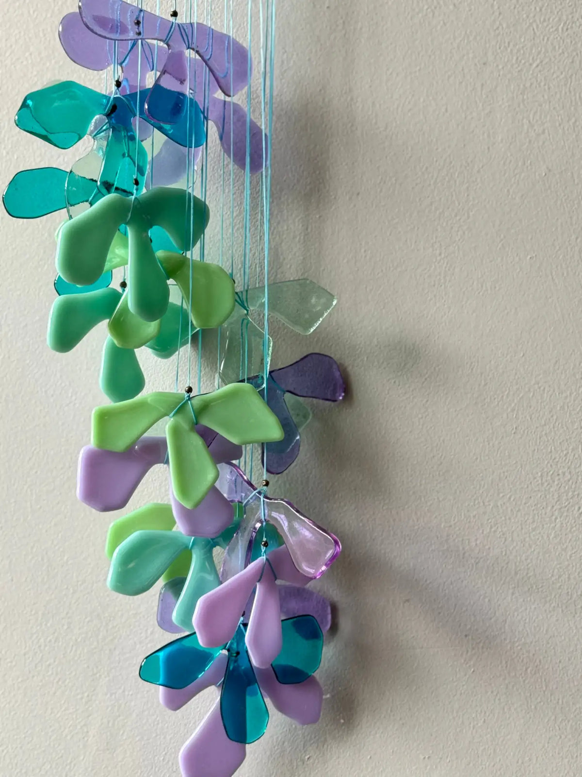 A colorful glass wind chime with translucent, leaf-shaped pieces in shades of purple, teal, and green hanging from thin strings.