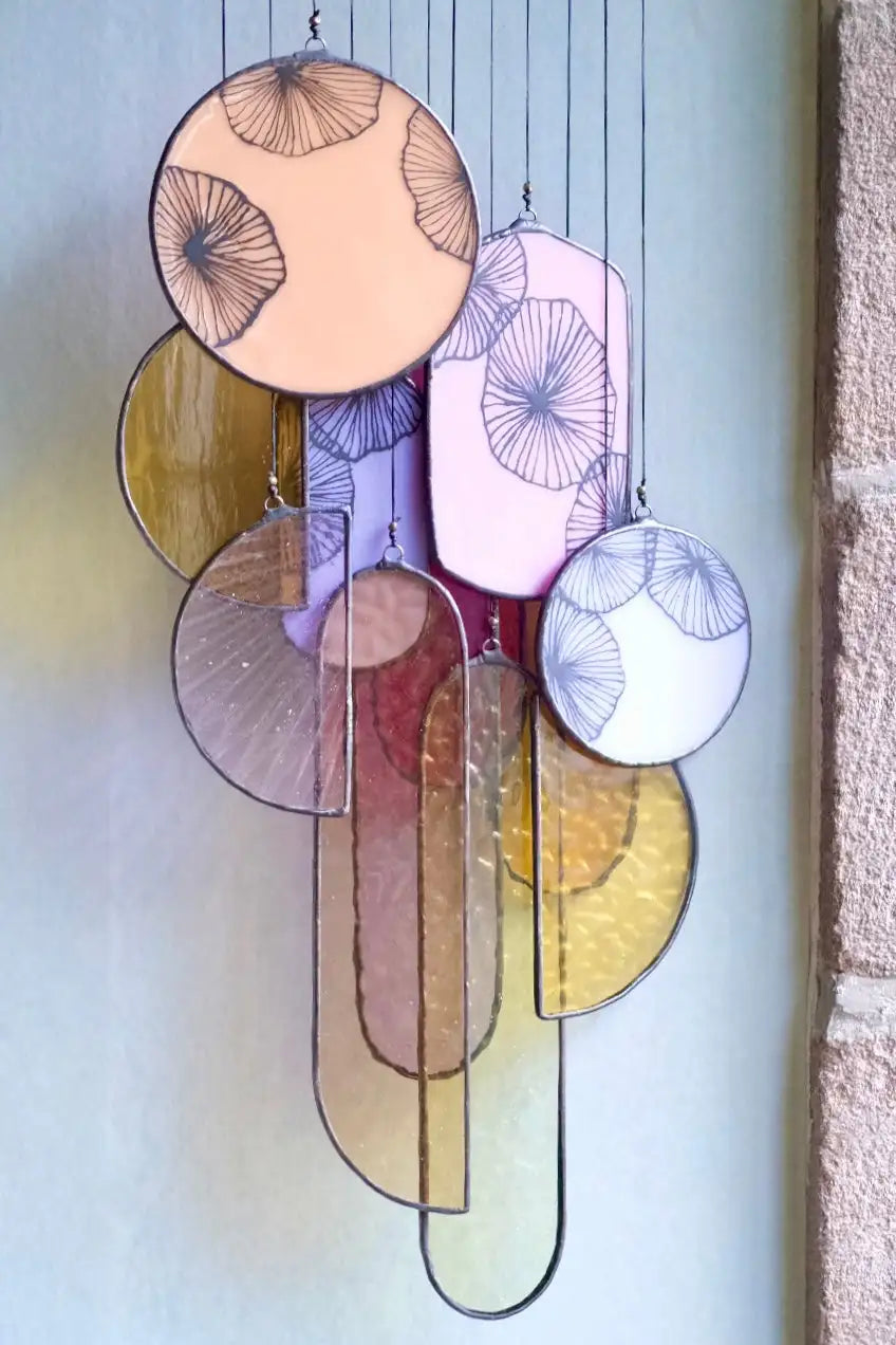 A colorful stained glass hanging art piece featuring circular and oval panels with fan-like patterns in soft pastel hues.