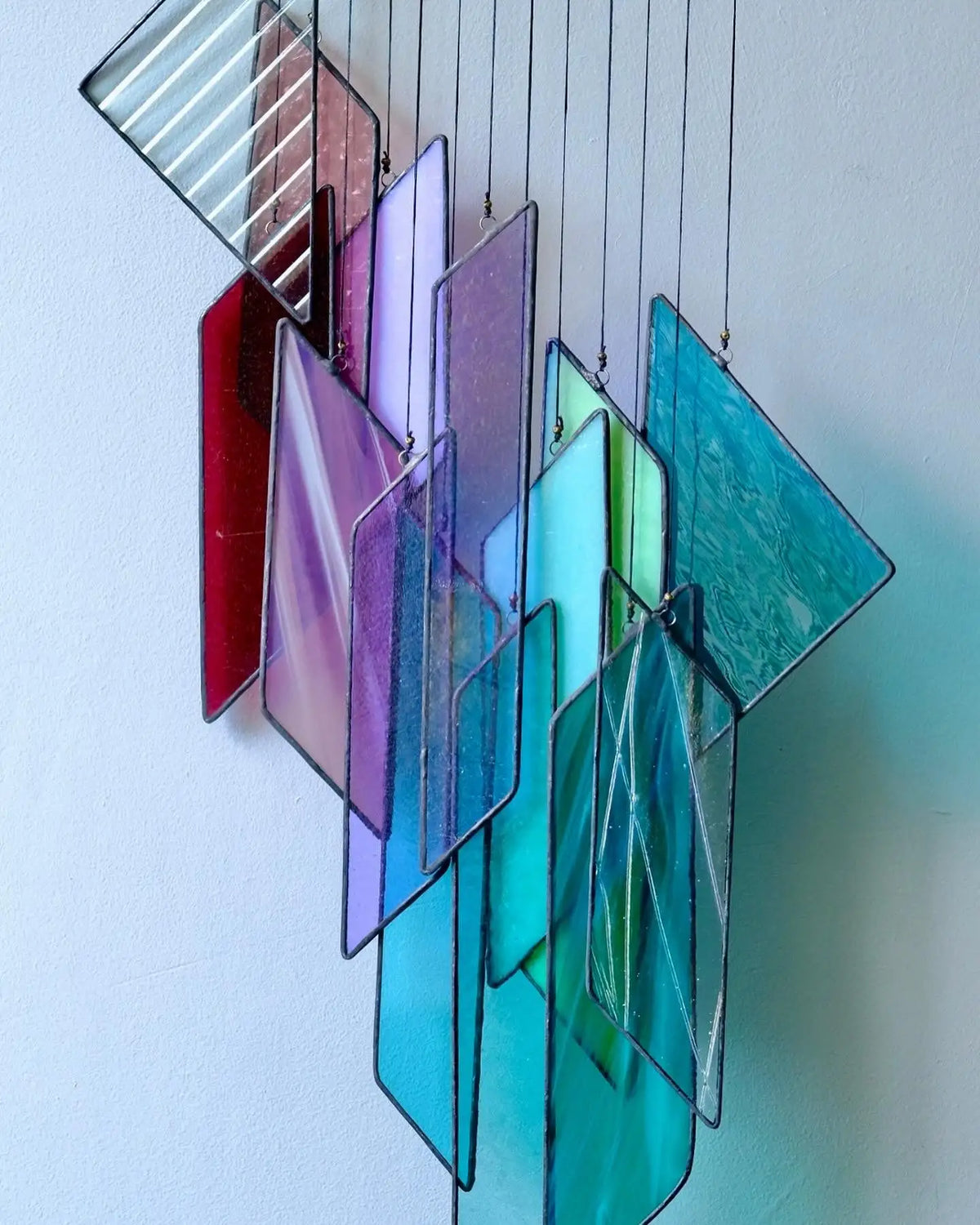 A colorful stained glass hanging art piece featuring rectangular and triangular panels in shades of red, purple, blue, and teal.