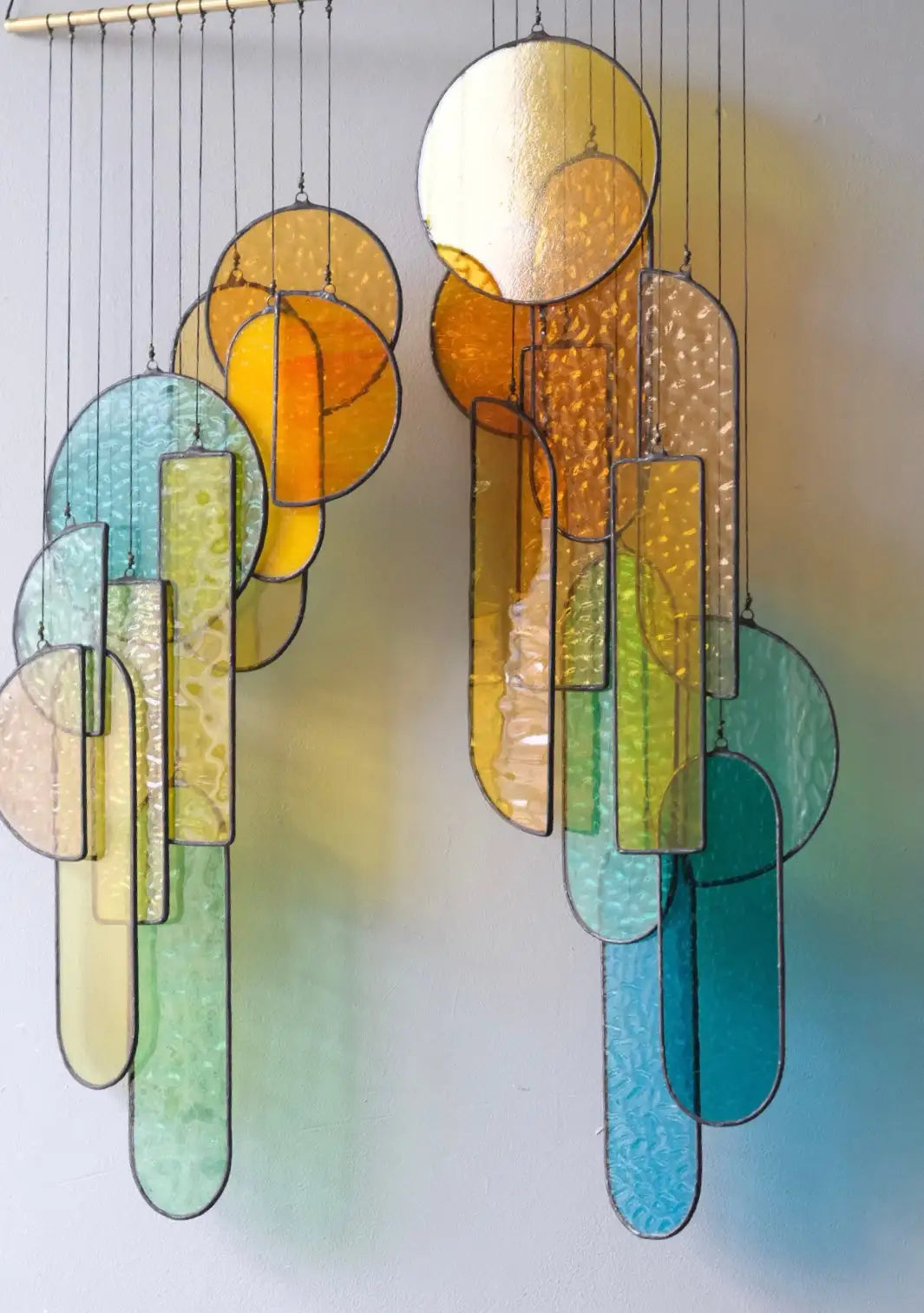 A colorful stained glass wind chime featuring circular and rectangular pieces in shades of yellow, orange, green, blue, and teal.