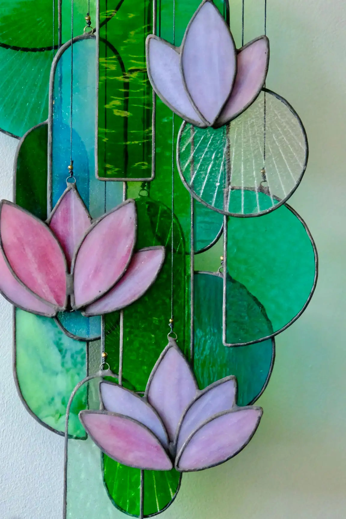 A delicate stained glass wind chime featuring pink and lavender lotus flowers with green lily pads, crafted from colorful leaded glass panels.