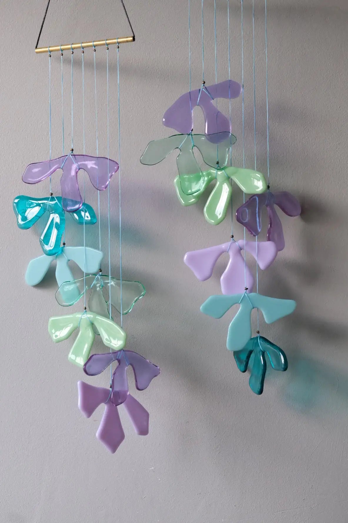 A delicate, translucent glass wind chime featuring abstract, flowing petal-like shapes in soft pastel hues of lavender, mint green, and teal.