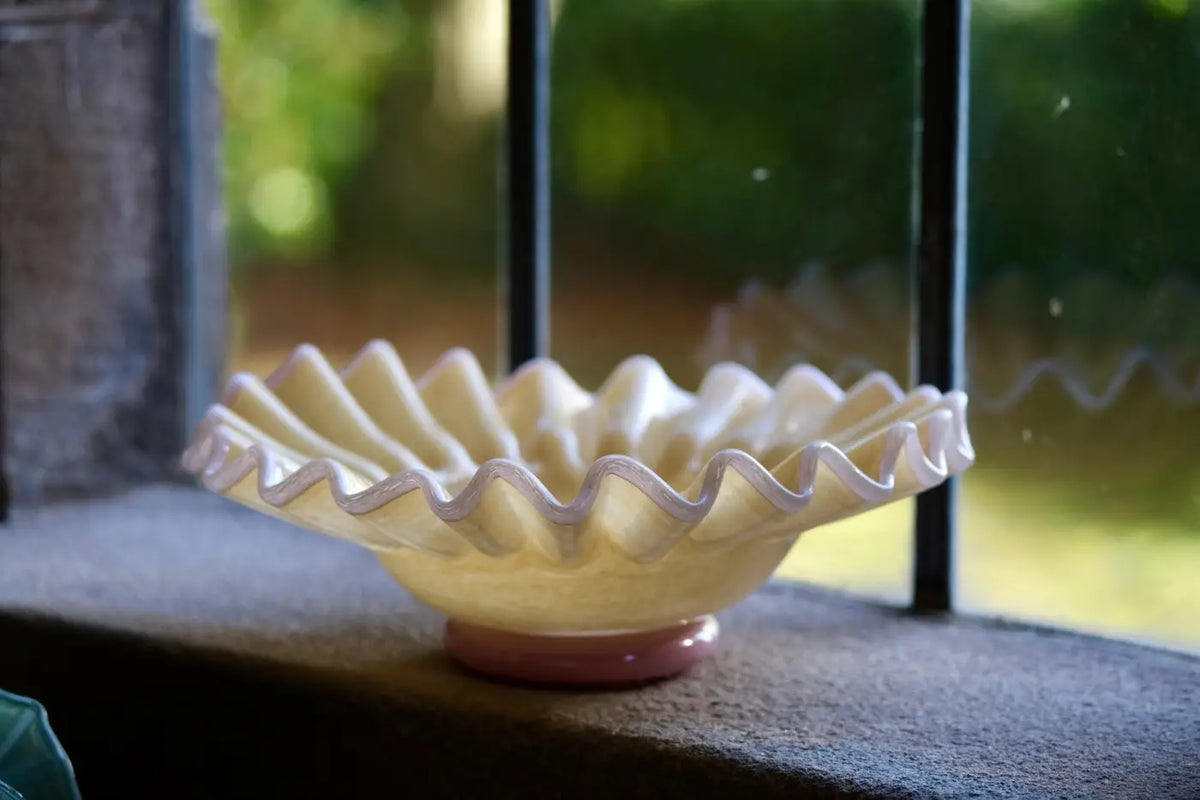 Elegant glass dish featuring a cream-colored glass bowl with a wavy rim and lavender accent on a pink base