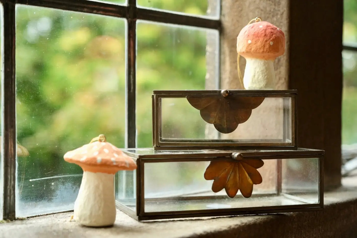 A ceramic mushroom ornament with a pinkish orange cap and white stem in a set of 2 glass trinket boxes