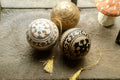 Hand painted paper mache baubles with intricate white and black floral patterns on a natural wood base with golden tassels