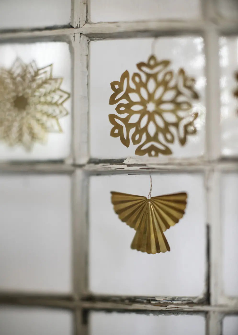 Handmade brass snowflake ornament set of 3 with golden paper snowflake hanging from a windowpane
