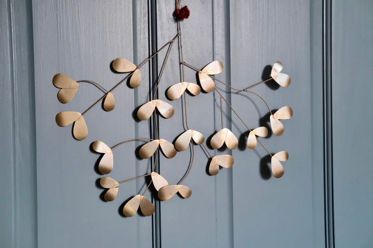 Handmade iron mistletoe wreath with delicate gold-toned metal and heart-shaped leaves hangs from red ribbon