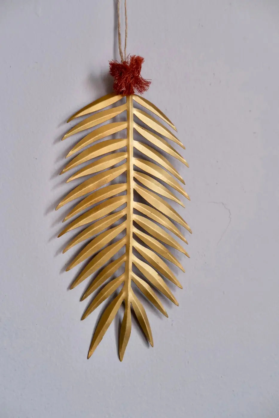 Handmade palm leaf decoration featuring a golden metallic palm frond wall hanging with a red tassel at the top