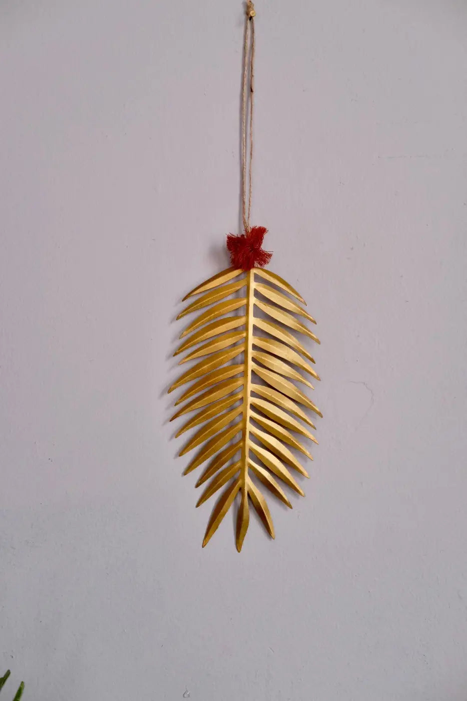 Handmade palm leaf decoration with a golden metallic finish and a red tassel at the top