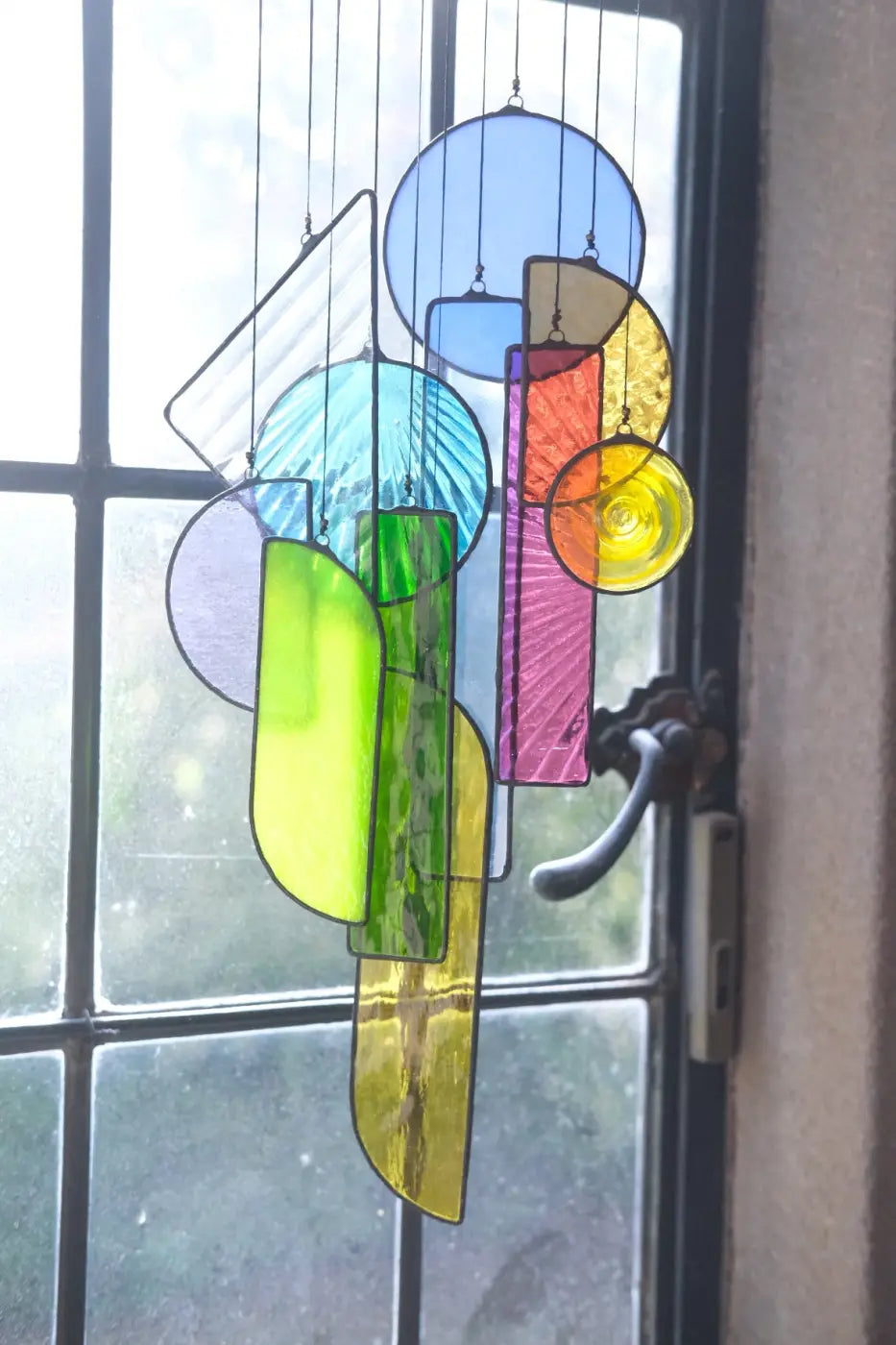 A vibrant geometric stained glass wind chime with translucent blue green yellow pink and orange panels for sun catching