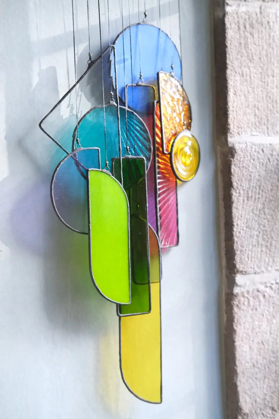 A vibrant multi-colored stained glass wind chime with geometric shapes in blue green yellow pink and orange by Lawrence 2
