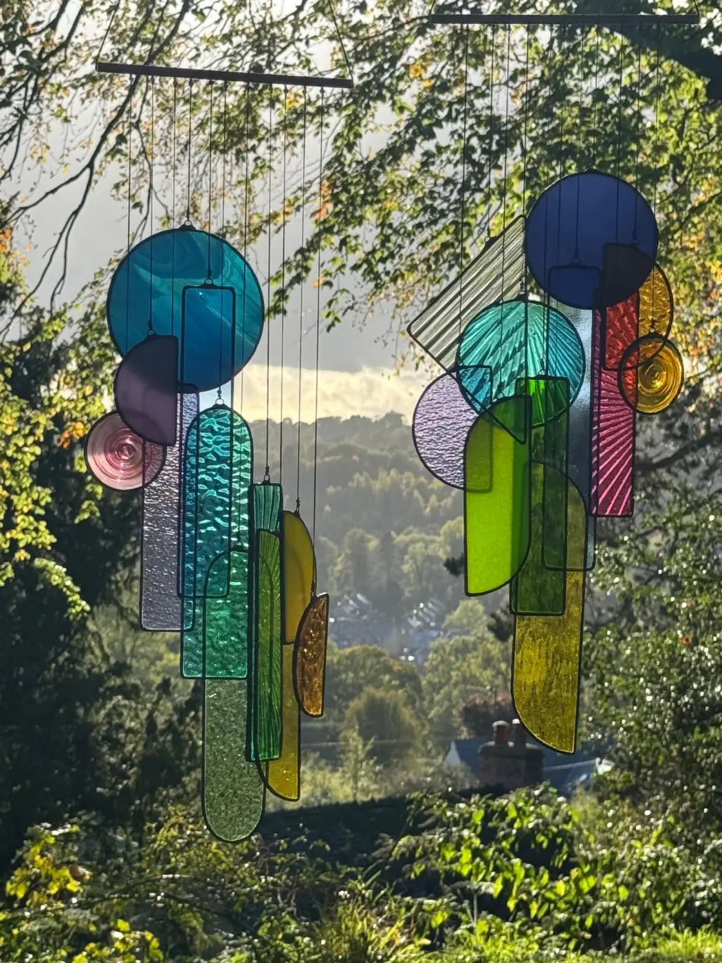 Vibrant multicolored stained glass sun catcher wind chime with geometric and organic shapes suspended by strings