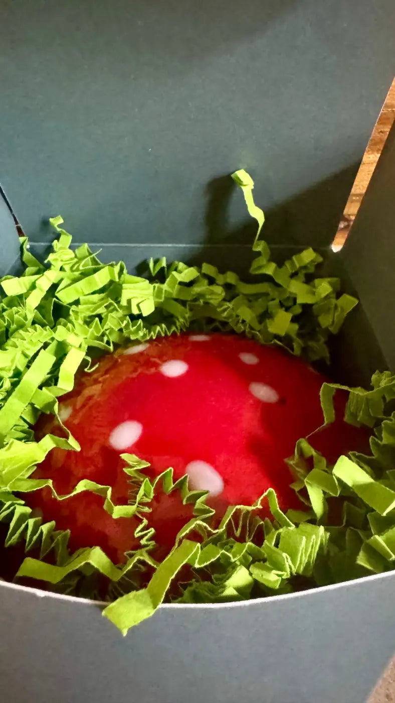 LumieShrooms handmade mushroom candle in plush red with white polka dots nestled in green shredded paper box