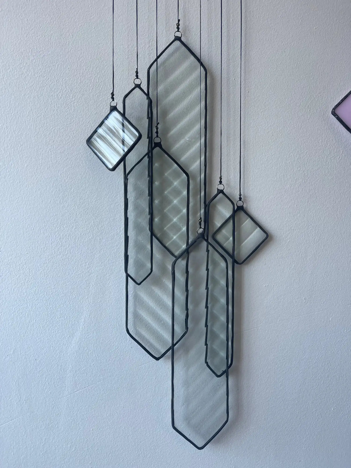 A modern geometric stained glass hanging wall art piece with black metal frames and translucent, subtly textured panels.