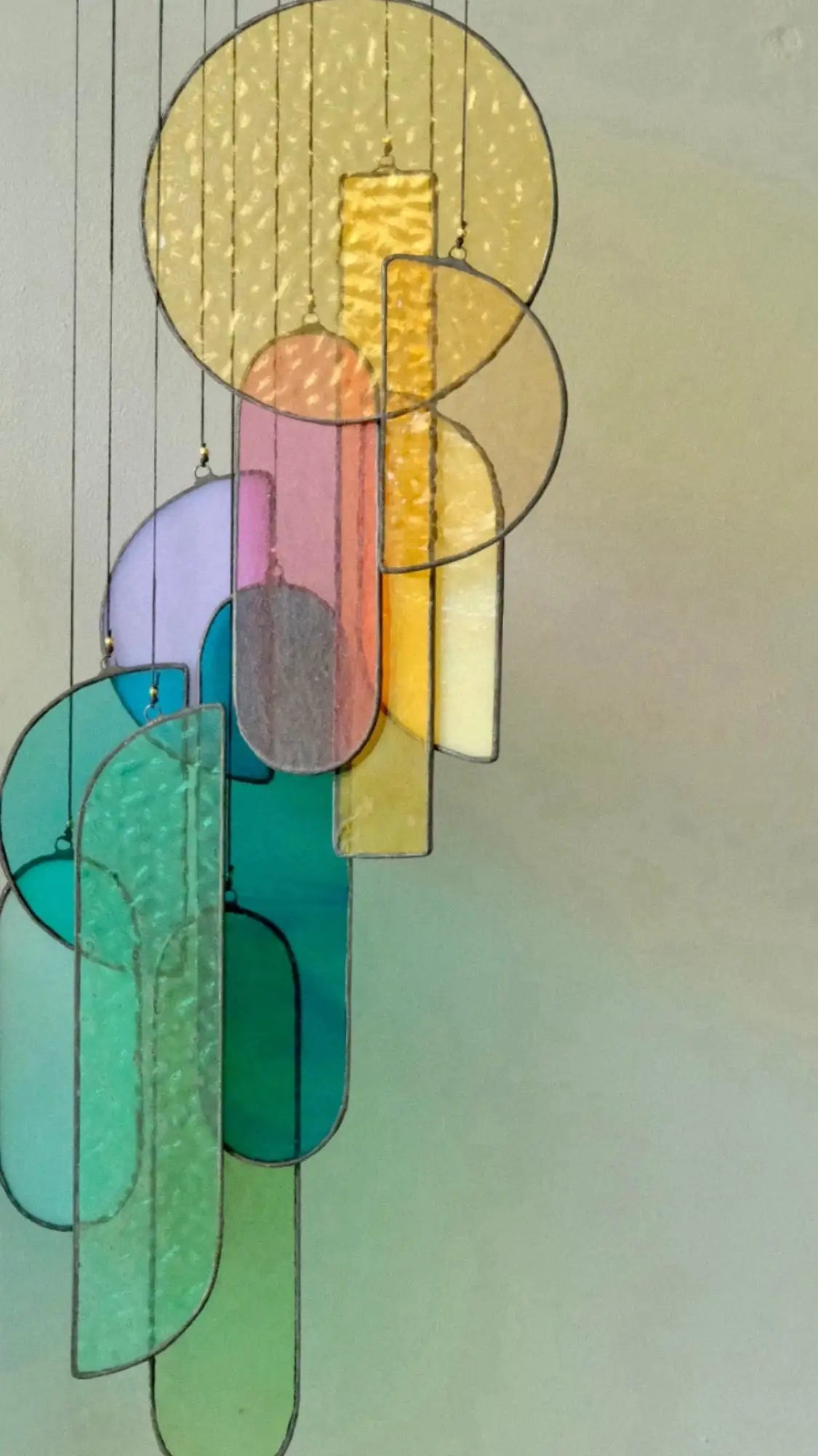 A modern stained glass chandelier featuring overlapping geometric shapes in vibrant hues of yellow, pink, teal, and purple.