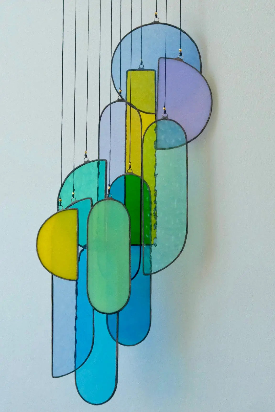 A modern stained glass chandelier featuring translucent panels in shades of blue, green, yellow, and purple, arranged in an abstract geometric pattern.