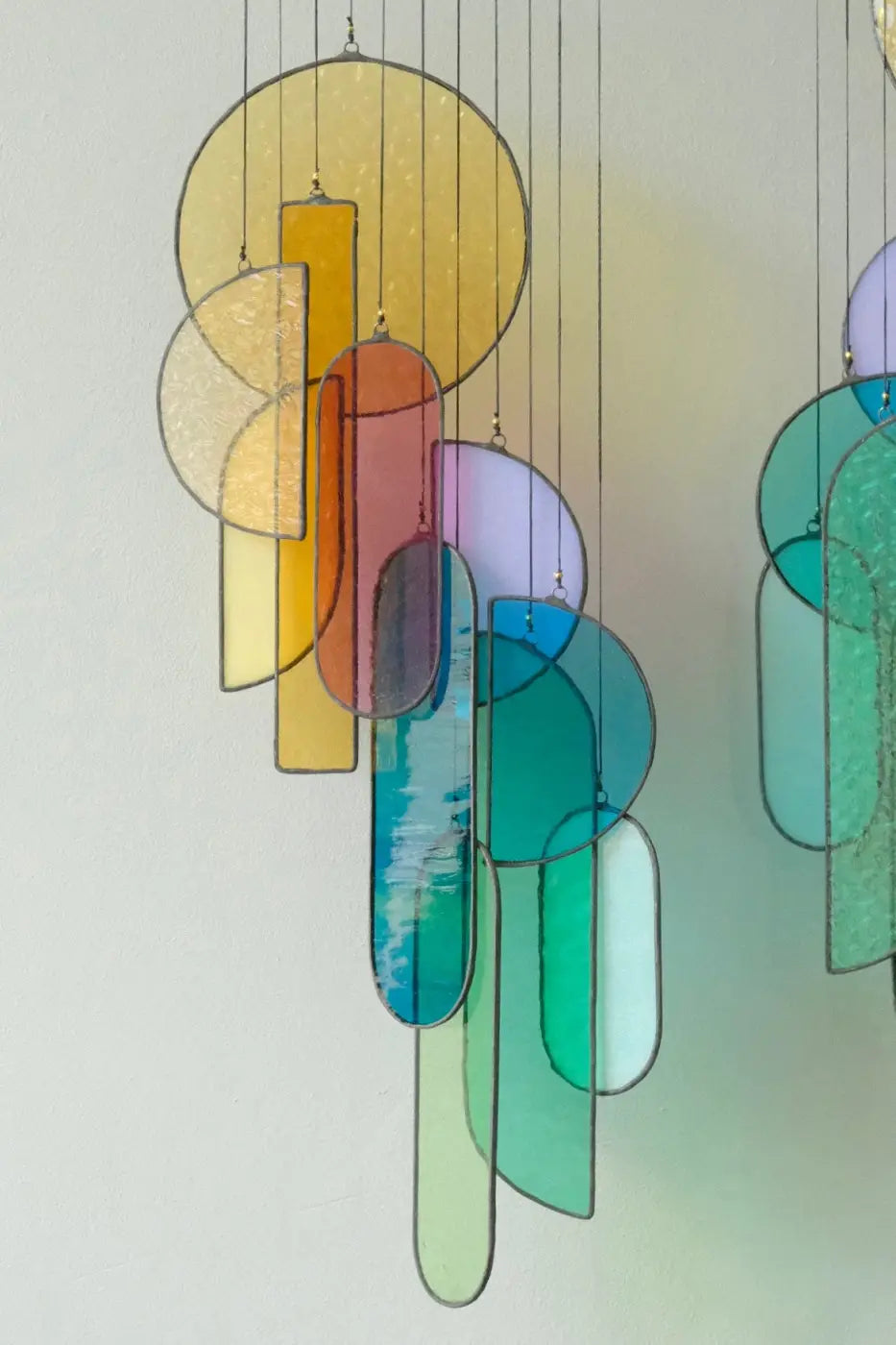 A multicolored stained glass sun catcher made of various geometric shapes, hanging by strings against a light source which is causing the glass to glow.
