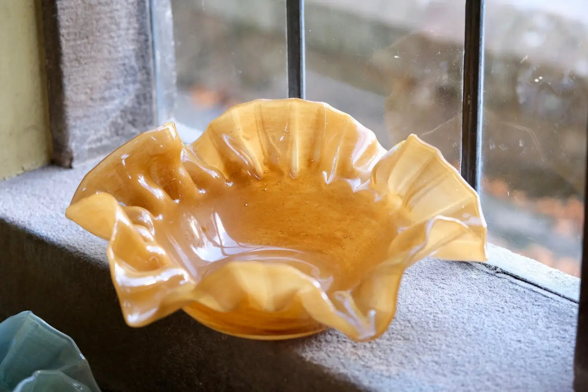 A translucent amber ruffle glass bowl with a petal-like rim and smooth glossy finish in caramel color