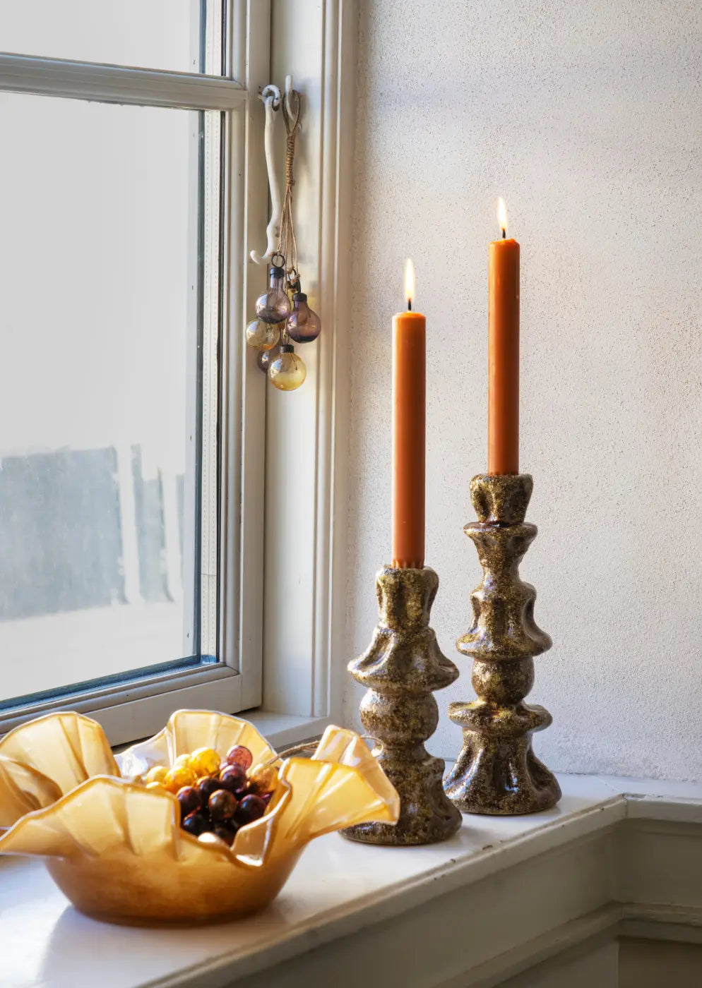 Two tall textured ceramic candle holders with speckled brown gold finish hold lit orange candles for decor
