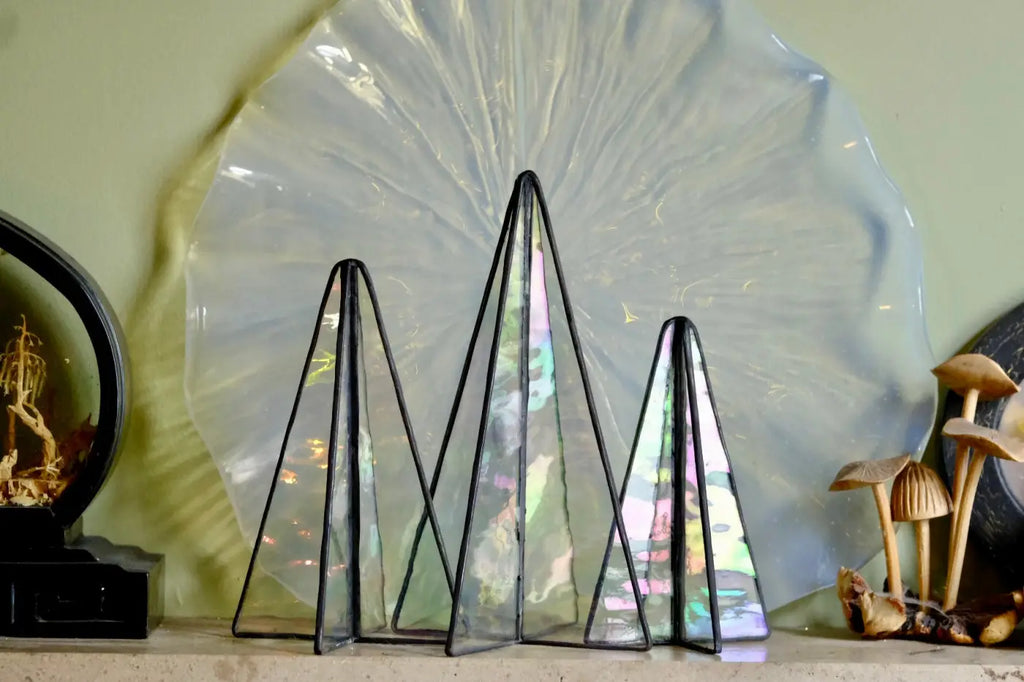 Three triangular glass terrariums with black metal frames and iridescent stained-glass panels reflecting rainbow hues