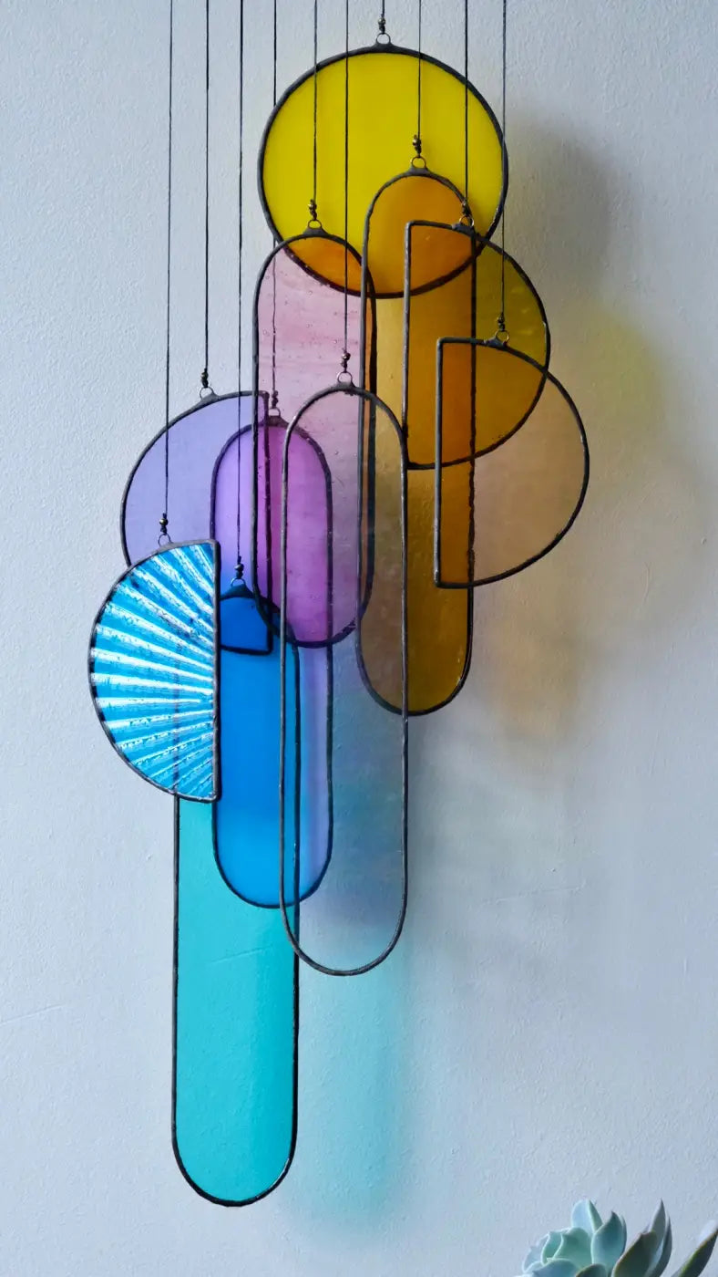 A multicolored stained glass sun catcher with various geometric shapes, hanging by a brass bar with linen cord against a neutral background.