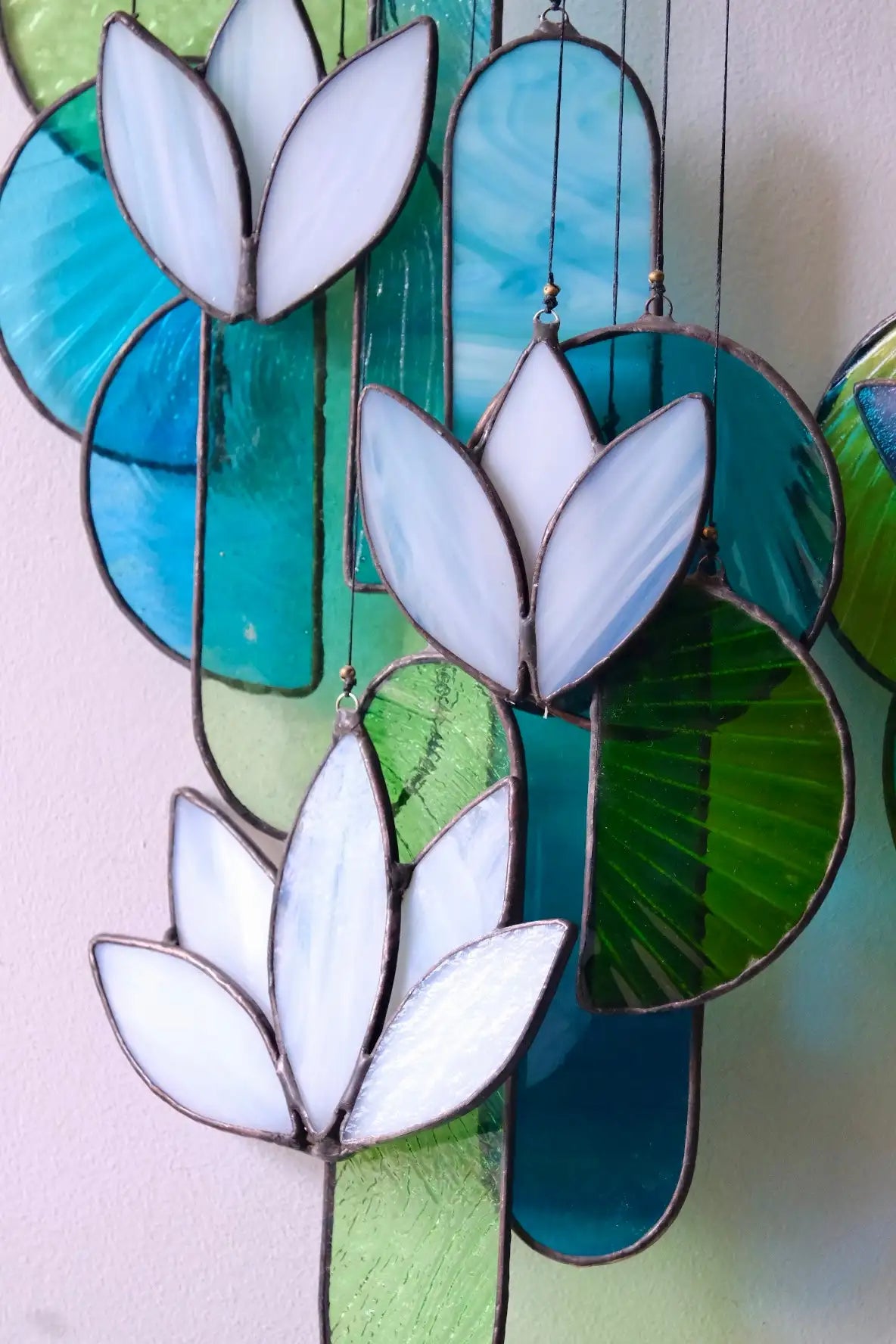 Stained glass hanging art featuring white lotus flowers and green-blue cactus shapes.