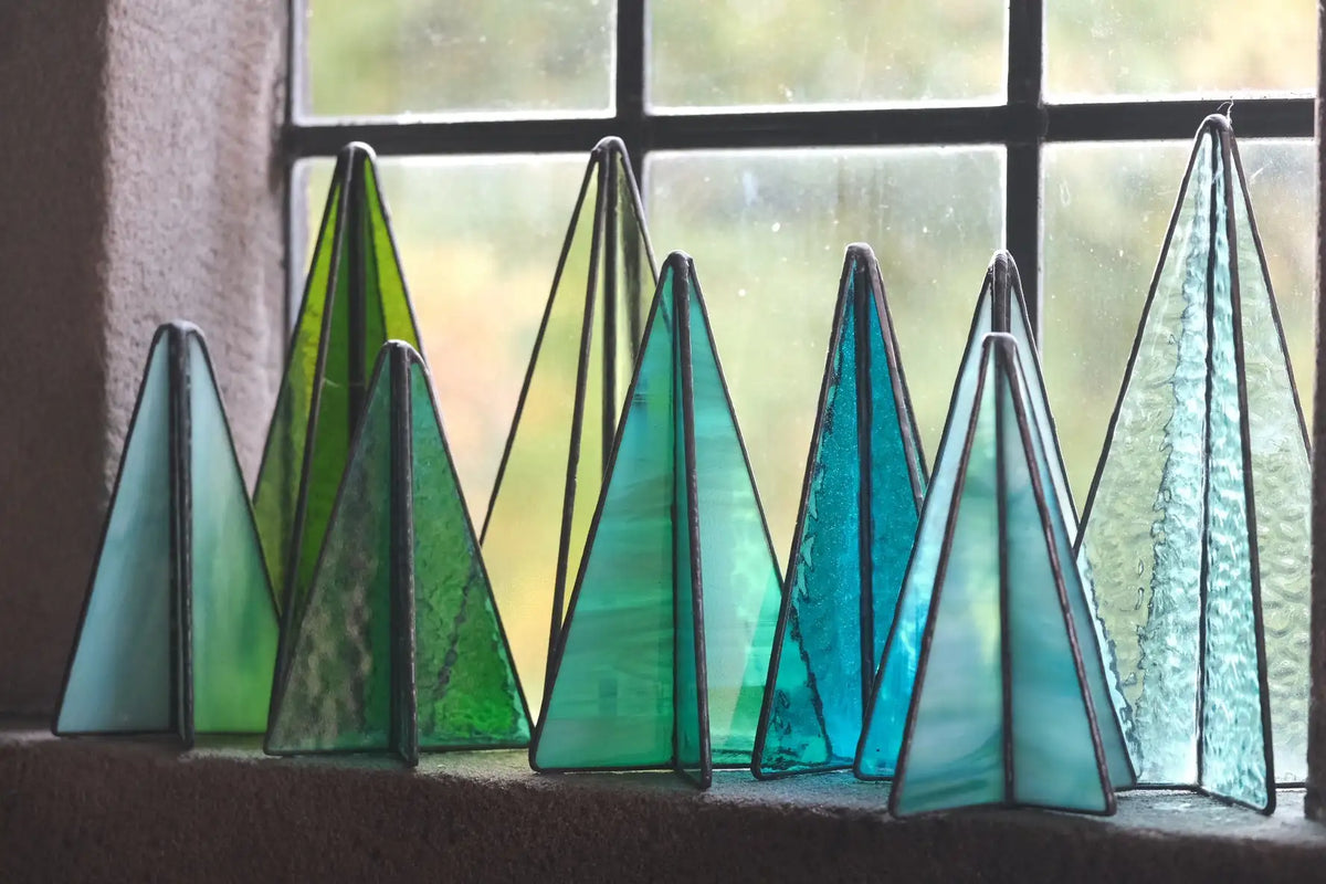 Stained glass christmas tree ornaments in varying shades of green and blue, framed with dark metal.