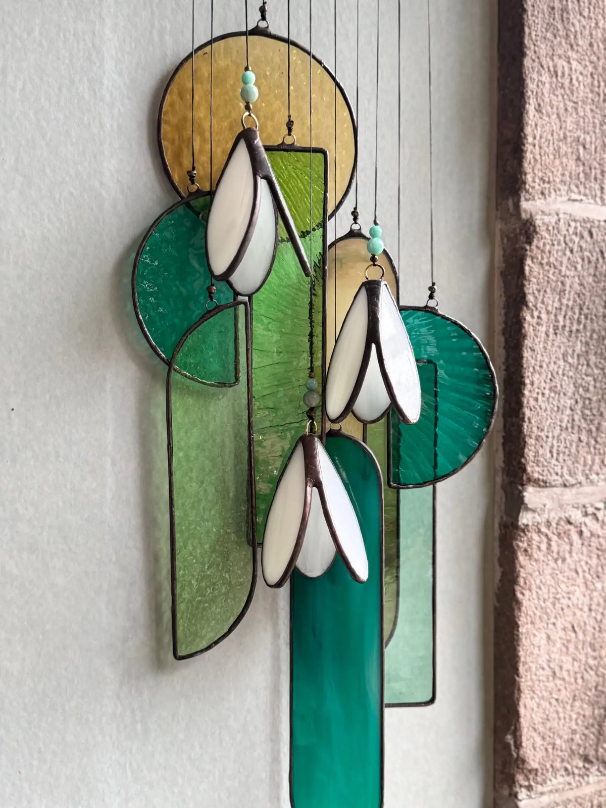 A hanging stained glass suncatcher featuring stylized snowdrop flowers in white and green with gold accents.