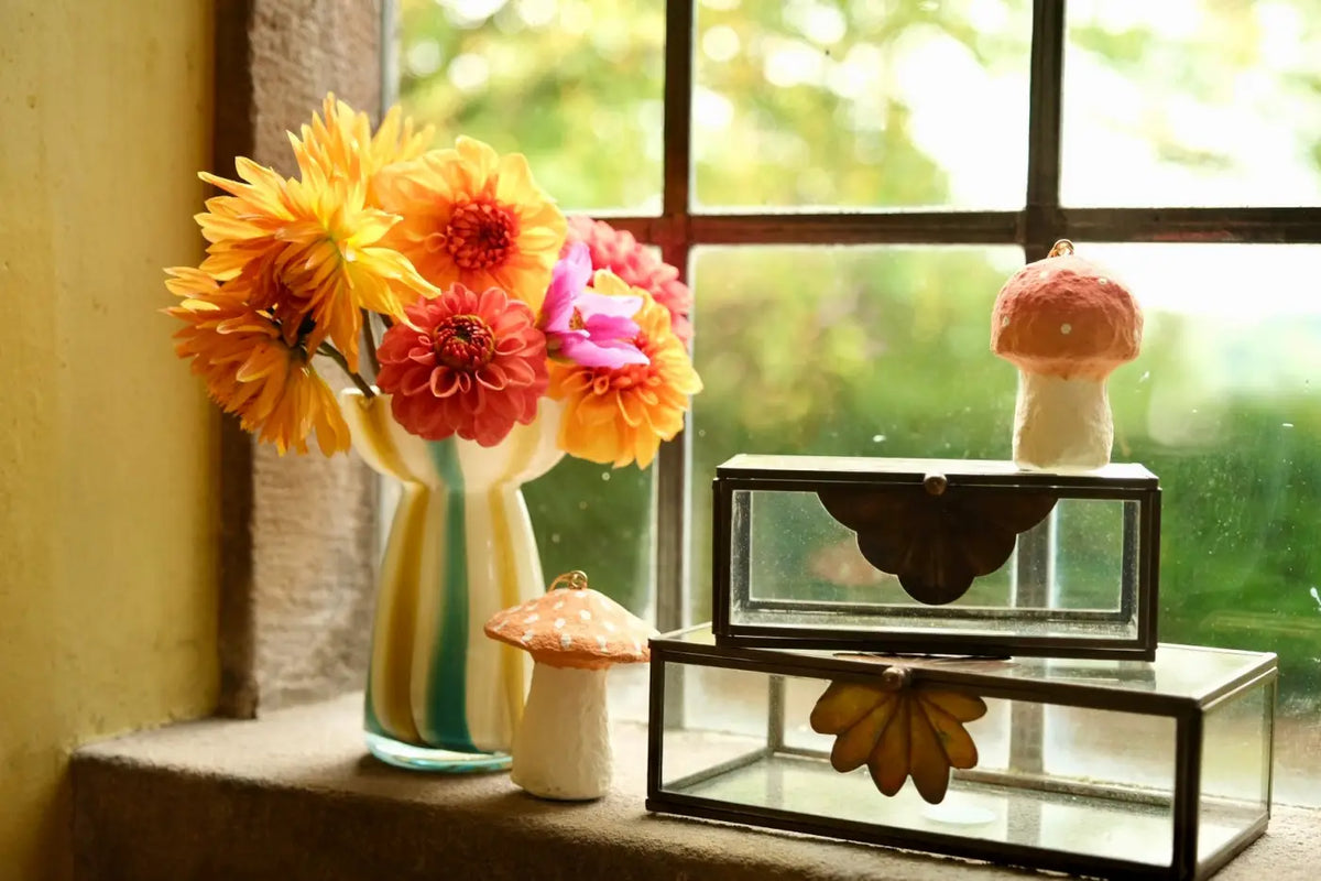 A vibrant bouquet of orange red and pink dahlia flowers in a striped yellow and green glass vase