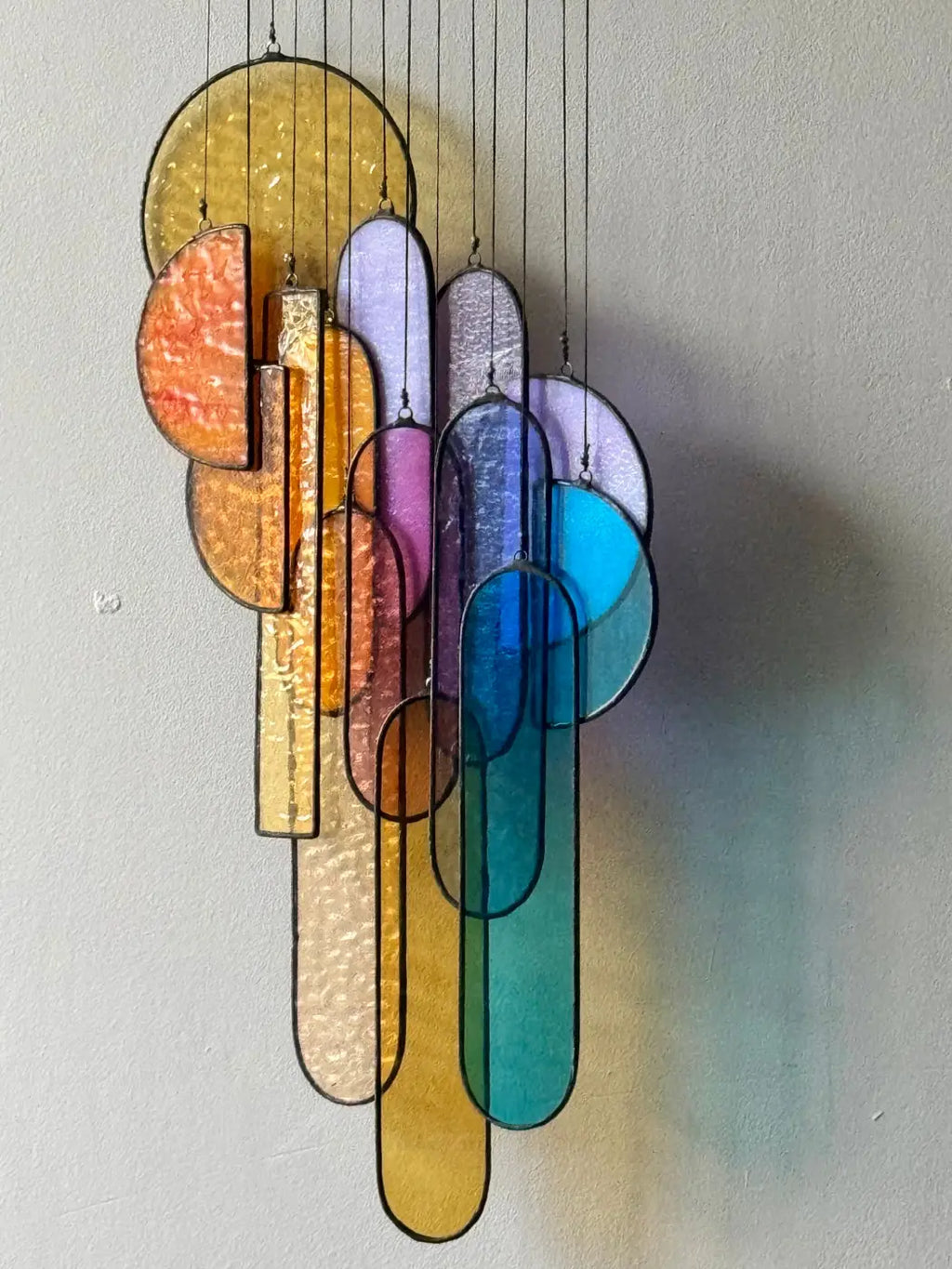 A vibrant multi-colored stained glass sun catcher with abstract geometric shapes in yellow orange purple blue and teal
