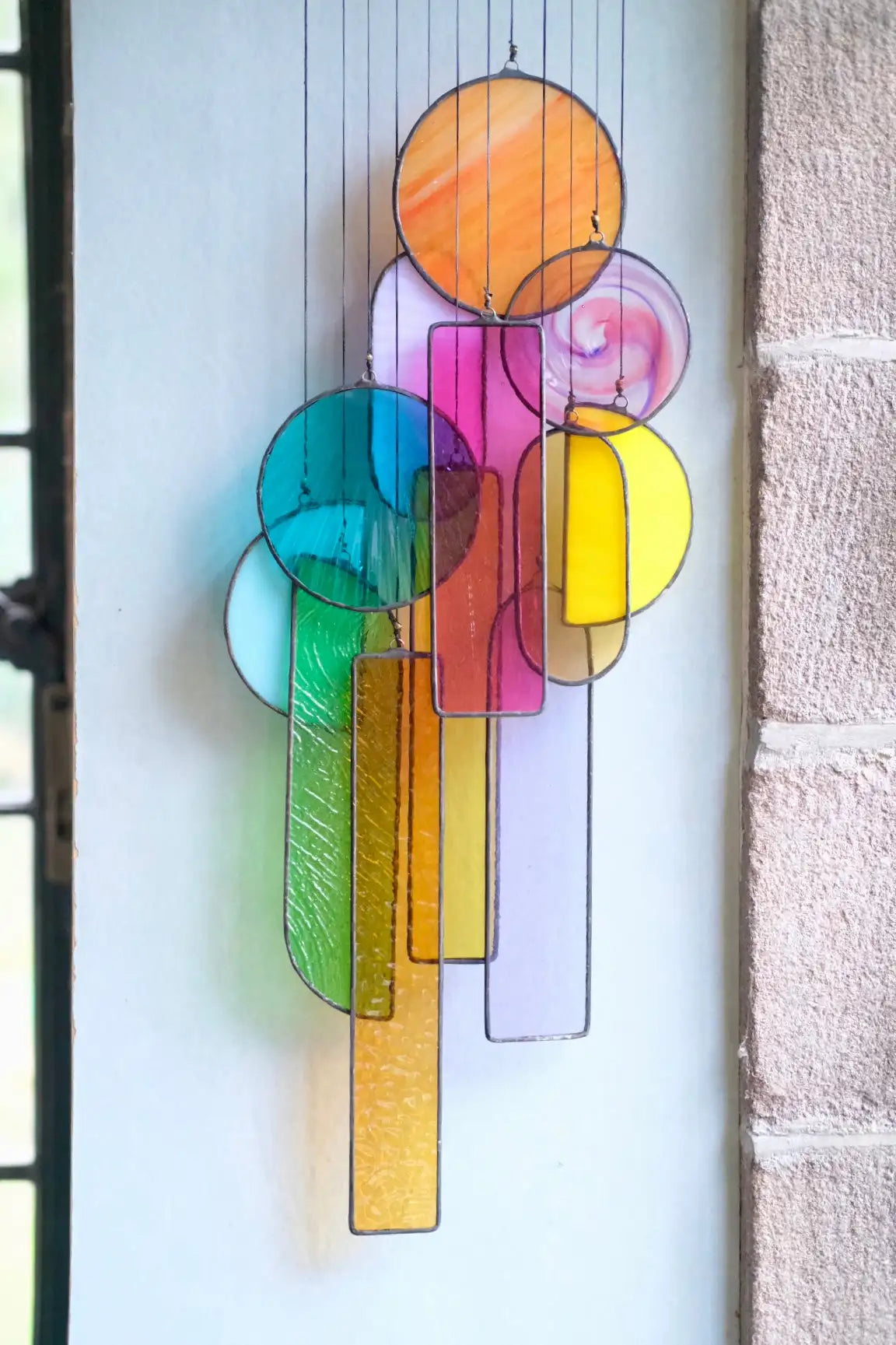 A vibrant, multi-colored stained glass hanging art piece featuring circular and rectangular shapes with a rainbow gradient effect.