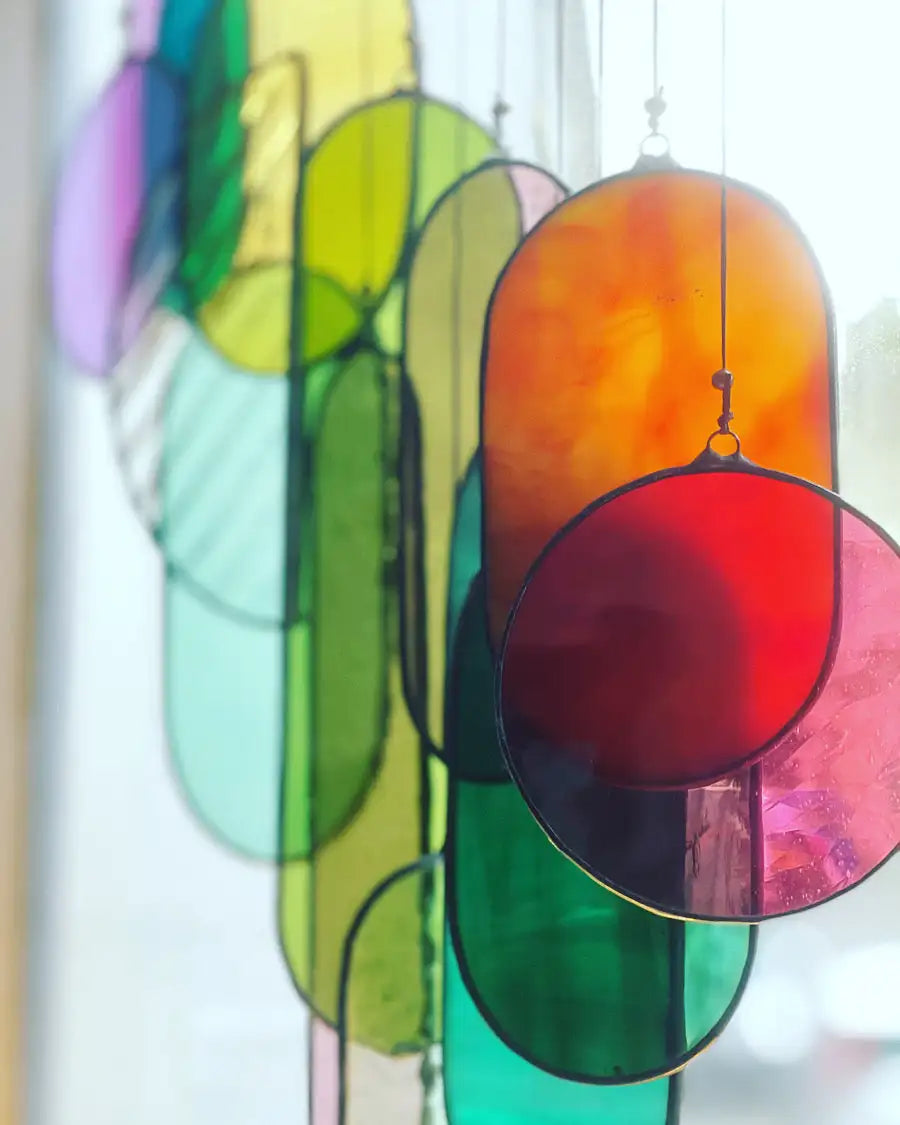 A vibrant, multi-colored stained glass sun catcher featuring oval and circular pieces in shades of orange, red, green, yellow, and purple.