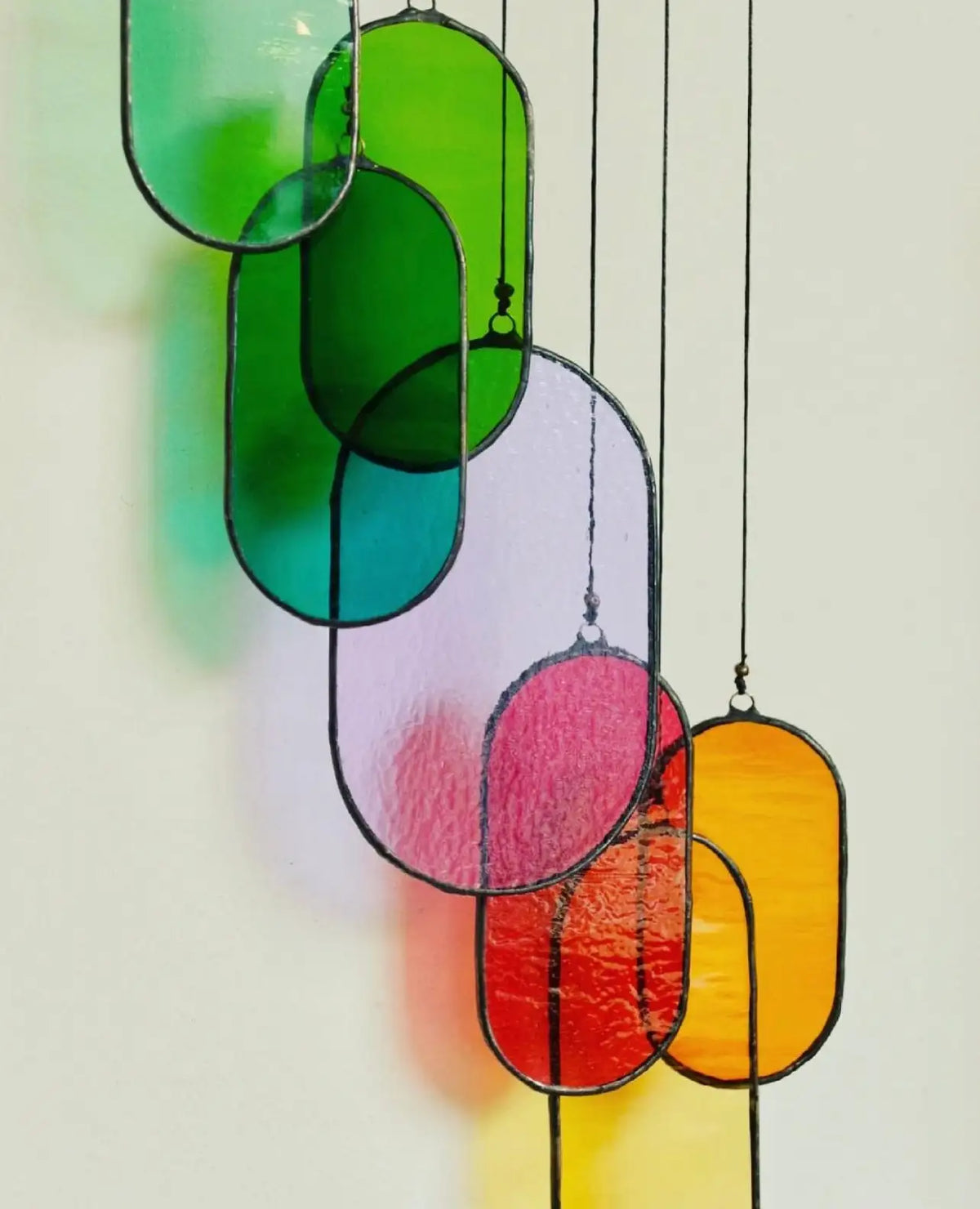 A vibrant, oval-shaped stained glass hanging decoration featuring a gradient of green, teal, pink, red, and yellow hues with black leaded edges.