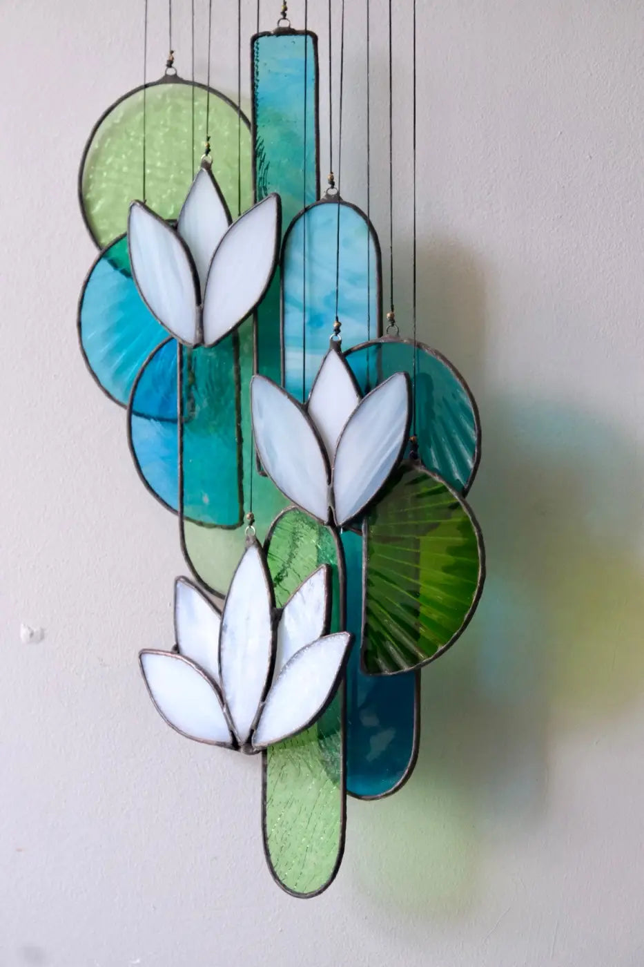 White lotus stained glass hanging art featuring white lotus flowers with teal and green circular and rectangular panels