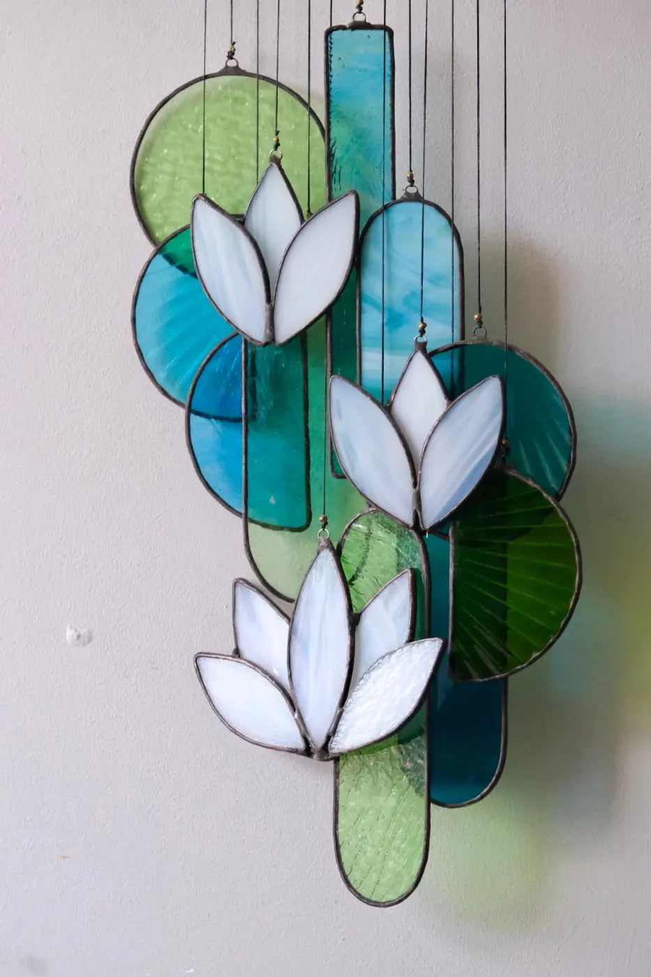 White lotus stained glass hanging art featuring white lotus flowers on teal green and blue circular and rectangular panels